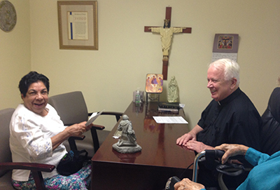 St. Mary Magdalen parishioner Mercedes Rodriguez reacts to receiving a 0 Heart of Christmas gift card from her pastor, Father Bernard Kirlin. Rodriguez, 73, is part of a family of two adults and three children trying to make ends meet on one part time job.