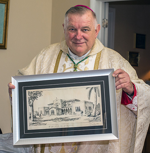 Archbishop Thomas Wenski holds a drawing of the original architectural sketch for St. Anthony School which principal Tery Maus presented to him.