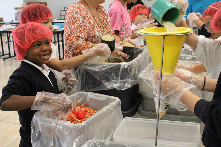 A second grader smiles as he prepares to pour in dried vegetables to the meal bag mix.