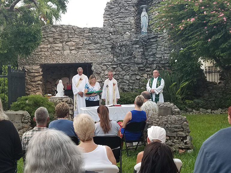 A parishioner proclaims one of the readings as Father John Baker, center, accompanied by Deacon Peter Batty, left, and Father Juan Rumin Dominguez, right, celebrates 7 a.m. Mass Sept. 7 at the grotto of Our Lady of Lourdes outside the Basilica of St. Mary Star of the Sea.