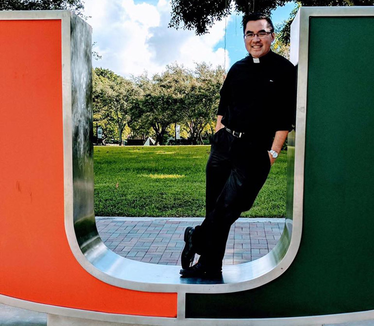 Going back to the U: Father Phillip Tran, a 2008 alumnus, poses on the iconic orange and green U at the University of Miami. Father Tran is the school's new full time Catholic Campus ministry chaplain.