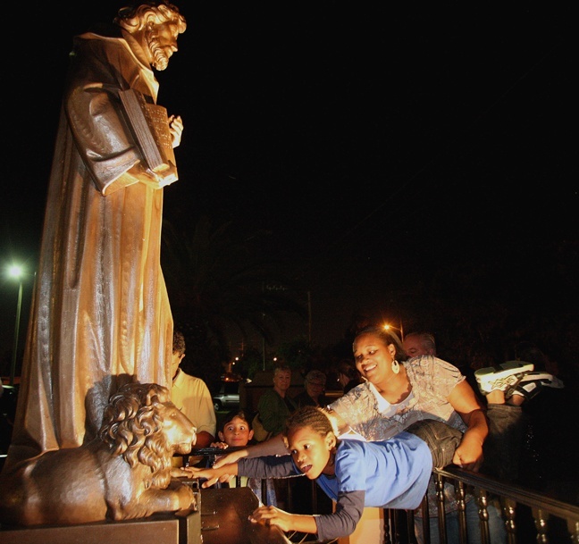 Regine Lamaute helps Khaman Foster, 6, reach out to touch the newly-dedicated bronze statue of St. Jerome, which is inside a fenced-in area in front of the Fort Lauderdale church.
