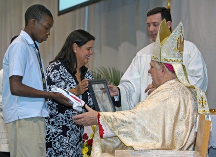 Pace senior Moise Jerome and Monica Lauzurique of the lay missionary group Amor en Accion, present the archbishop with symbols of the high school's commitment to service during the offertory.