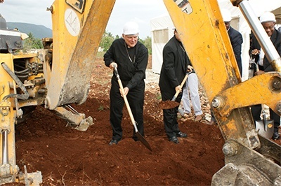 Archbishop Wenski shovels dirt under a large earthmover during the groundbreaking for the new multipurpose building in Jacmel.