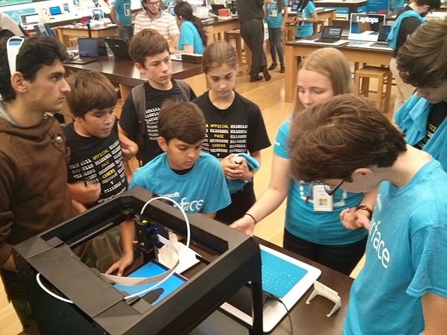 Geek Week attendees Antonio D’Agenzio, Joshua Dubon, Noah Florin, Eduardo Gabriel, Alexandra Perez, Andrew Sanchez, and Alexander Moore watch as a Microsoft Store employee (third from right) demonstrates a 3D printer.