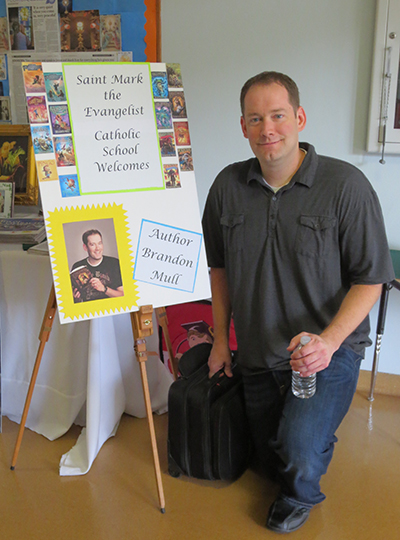 Author Brandon Mull poses with the welcome board created by St. Mark faculty.