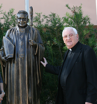 Father Brendan Dalton poses next to the statue of Archbishop Edward A. McCarthy, the school's namesake.