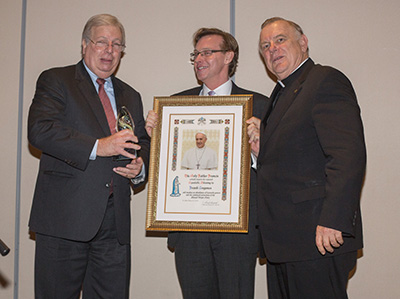 Attorney Frank Angones, left, a Pedro Pan immigrant, receives his New American Award from Randy McGrorty, CEO of Catholic Legal Services, and Archbishop Thomas Wenski.