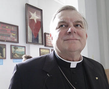 Con la bandera cubana detrás, el Arzobispo Thomas Wenski observa la nave del Santuario de Nuestra Señora de La Caridad de El Cobre, durante la peregrinación en marzo del 2012 coincidiendo con la visita del Papa Benedicto XVI a la isla. La visita del Papa Benedicto XVI, según algunos observadores, ayudó a consolidar el papel de la Iglesia cubana como un intermediario de confianza entre los gobiernos de Cuba y los EE.UU.