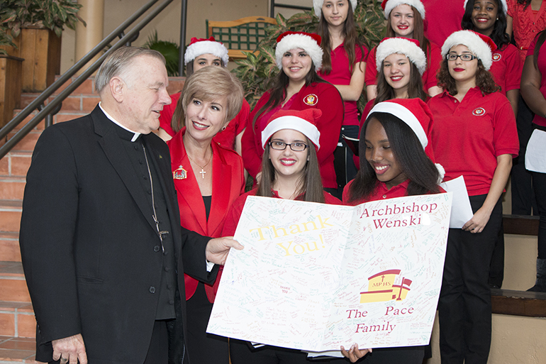 Archbishop Thomas Wenski receives a thank you card for the 650,000 dollar donation toward new roofs, from Msgr. Edward Pace High freshmen Leticia Saladrigas, center, and Marie Prisca Maymaurice, right, as Principal Ana Garcia looks on.