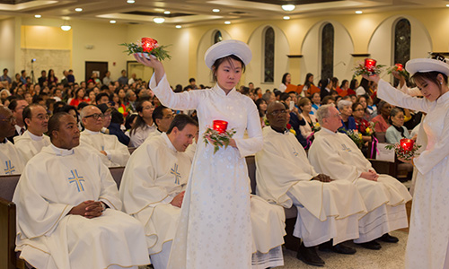 Members of Our Lady of La Vang's youth group dance in white ao dais, a traditional garment, while holding glass oil lamps.