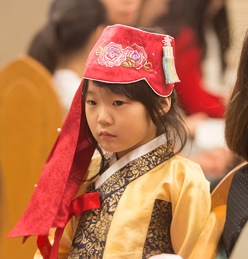 Claire Oh, 5, dressed in a traditional Korean dress and hat pays close attention during Mass.
