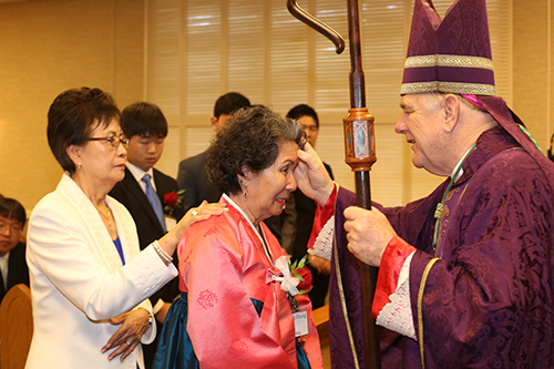 Elizabeth Kim witnesses as Archbishop Thomas Wenski confirms Ochang Chung during a Mass on Dec. 21 marking 30 years since the founding of South Florida's Korean Catholic community.