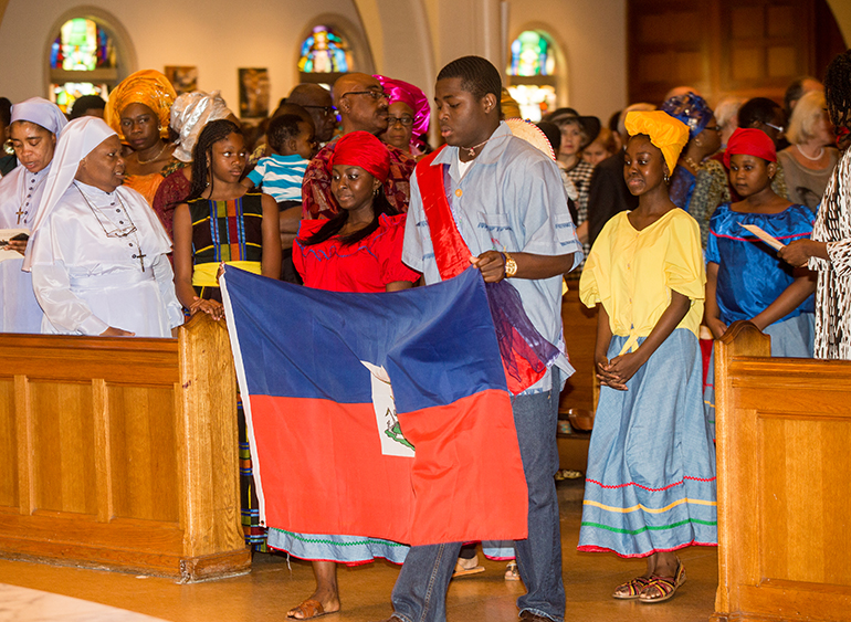 Regine Destin, 14, and Calvin Decius, 17, carry the Haitian flag into the cathedral during the entrance procession.