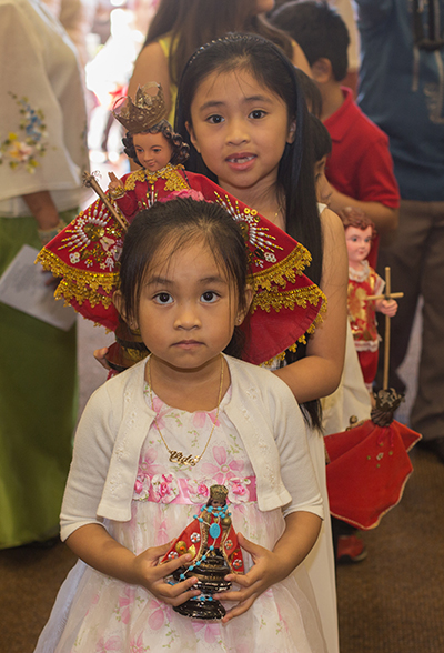 Honey Labrada, 4, and her sister, Elizabeth Labrada, 6, line up to process into church carrying their Senor Santo Nino statues.