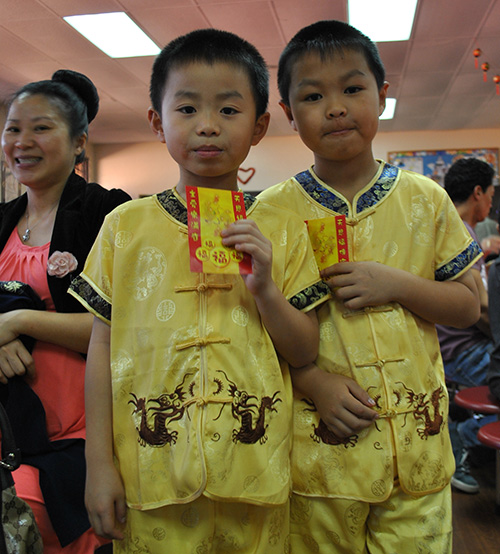 Brothers  Andrew and Ethan Jiang, aged 7 and 8, hold up their Hong Bao, or red envelopes, which contain a monetary gift and a holy card of Our Lady of China. Their mother, Yan C. Shi, looks on.