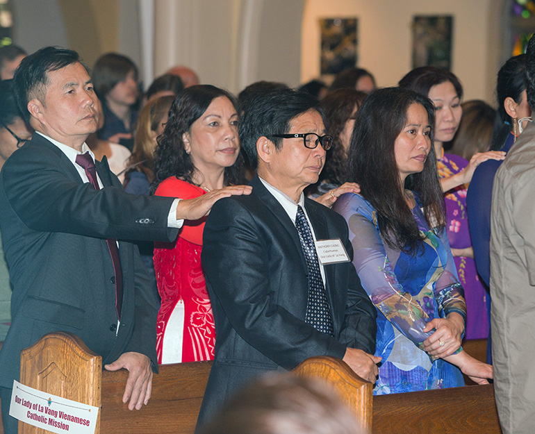 Sponsors from Our Lady of La Vang Vietnamese Catholic Mission place their hands on the shoulders of catechumens during the Rite of Election ceremony.