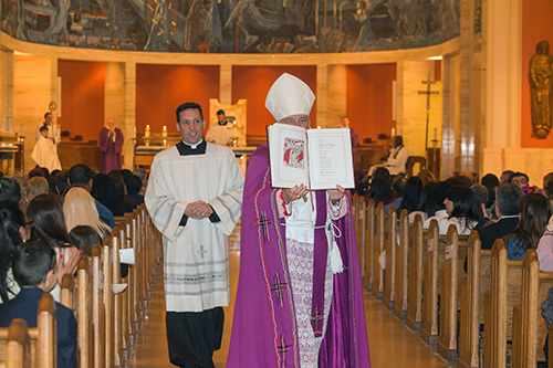 Archbishop Thomas Wenski carries the Book of the Elect through the center aisle of St. Mary Cathedral as his priest-secretary, Father Richard Vigoa, follows.