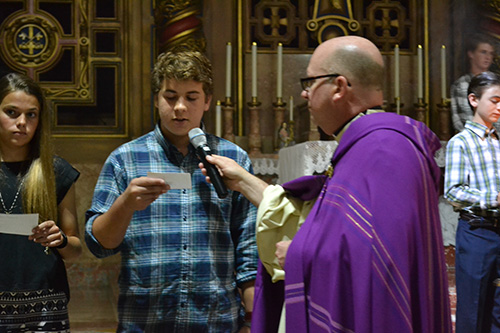Father Michael Davis, Little Flower's pastor, holds the microphone as Christian Alvarez, a student at St. Theresa School, reads a petition on behalf of a person or group who has suffered persecution in the Middle East.