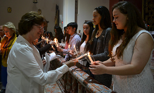 St. Theresa School students hold out their candles as other participants light theirs, during the interfaith prayer service for peace and the end of persecution and atrocities in the Middle East.