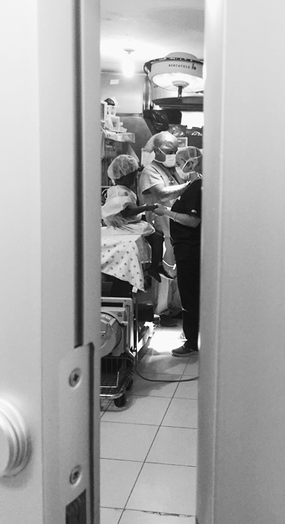 Peeking behind a door, Alexandra "Lexi" Thaller (right) can be seen in an operating room with a patient and anesthesiologist. Lexi, a junior at St. Brendan, accompanied her father  Dr. Seth Thaller and a team of UM/Jackson Hospital doctors to Port-Au-Prince, Haiti for Project Medishare.