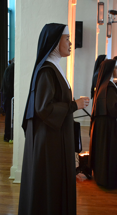 La Hna. Carmelita Mary Scholastica entra al Salón Comber de la parroquia Little Flower sosteniendo una vela para comenzar el concierto.