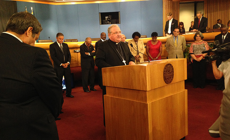 Miami Auxiliary Bishop Peter Baldacchino delivers the invocation at the start of the May 19 meeting of the Miami Dade County Commission. The occasion was the dedication by commissioners of a new logo that adds the words "In God We Trust." Bishop Baldacchino was one of three religious leaders who gave the invocation. The others were Rabbi Avrohom Brashevitzky, co-director of Chabad Jewish Center of Doral, and Rev. Steve Alessi, founding pastor of Metro Life Church in Doral.