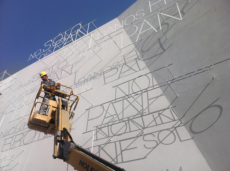 A workman puts the finishing touches on the exterior of the Vatican's 747-square-foot pavilion at the Milan Expo 2015. The words "Not by bread alone" convey the theme, a Gospel take on the Expo's focus, "Feeding the Planet, Energy for Life." Also written in 13 languages is the phrase: "Give us this day our daily bread."