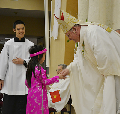 El Obispo Auxiliar de Miami, Peter Baldacchino saluda a Cathy Vu, la niña que representó a Vietnam durante el desfile de niños en trajes típicos de sus países de origen, por el 25 Aniversario de la Parroquia St. Martin de Porres.