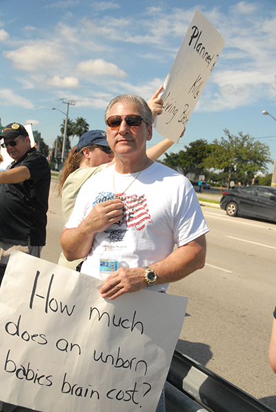 David Babbin, a parishioner at St. Elizabeth Ann Seton Church in Coral Springs, and also a member of the Knights of Columbus, Men's Ministry, and St. Paul Street Evangelization, touches his cross during the protest. While in high school, he and his then girlfriend decided to have an abortion. It affected him deeply, said the now father of two, including a child with Down Syndrome. "Why is it that when you don't want it, it's a clump of tissue, but then when you want it and the strip turns blue, it's a child and a life? It's the ultimate hypocrisy."