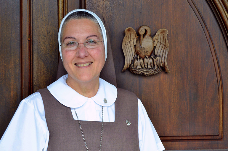 Mother Adela Galindo, who founded the Servants of the Pierced Hearts in Miami in 1990, stands beside the wood carving of the pelican, a major symbol for her community because of a belief that a mother pelican will pluck her own breast in order to feed her children.