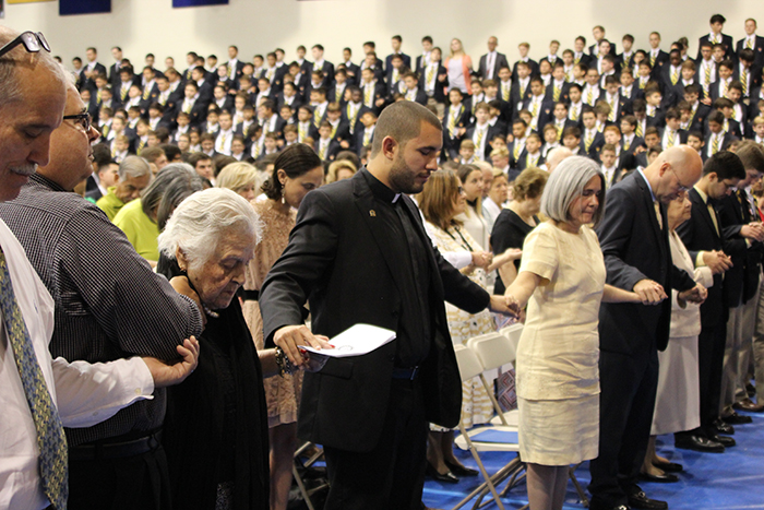 Belen Jesuit alumnus Michael Martinez holds hands with his family during the Our Father at the schoolwide Mass of the Holy Spirit where he made his first vows to the Society of Jesus, in front of the entire student body.