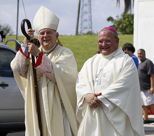 Archbishop Thomas Wenski and Auxiliary Bishop Peter Baldacchino look out at the lake behind the stage at C.B. Smith Park after vesting for Mass.