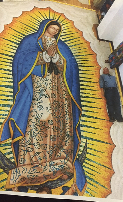 To get an idea of its size, a person lies next to the 26-foot-tall mosaic of Our Lady of Guadalupe as it was being crafted in Italy. The artwork is constructed by hand, from the finest Venetian glass “smalti” mosaic tiles. When the installation is complete at Our Lady of Guadalupe Church, it will be visible from the Turnpike.