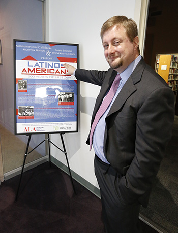 Rev. Jonathan Roach, interim dean of St. Thomas University's library, points to the poster for "Latino Americans: 500 Years of History," an exhibit which will be on display through May 2016 in the university's library.