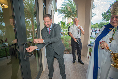 Tim Martin, Gantt Builders' director of operations, opens the door to the new building as Archbishop Thomas Wenski prepares to bless the facility.