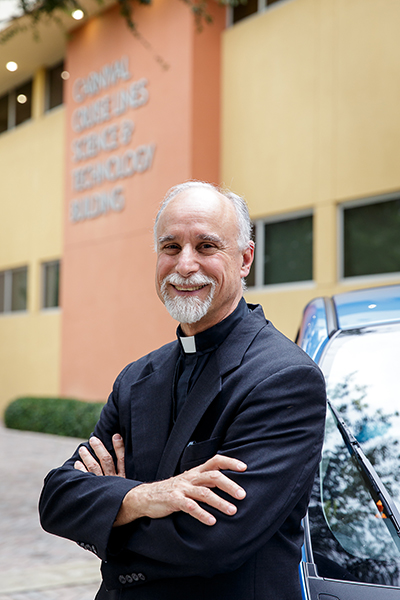 Father Alfred Cioffi poses in front of his electric car.