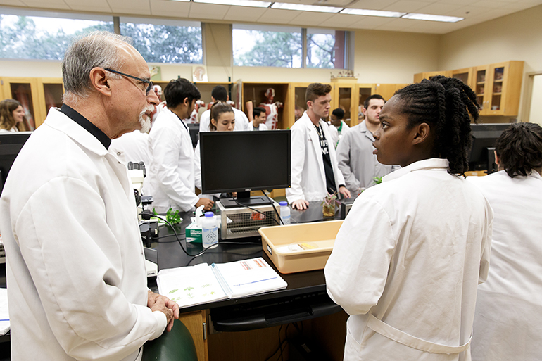 Father Alfred Cioffi helps students conduct biology experiments during a lab class at St. Thomas University.
