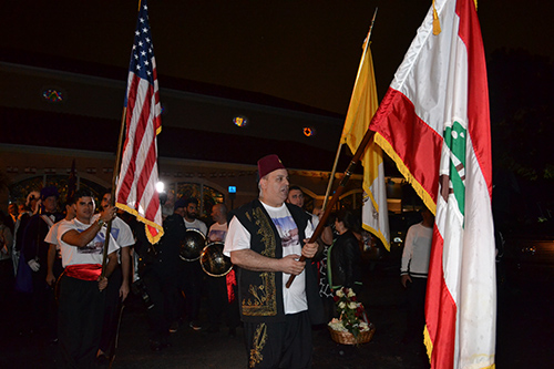 Los feligreses de Nuestra Señora del Líbano sostienen banderas libanesas, estadounidenses y del Vaticano mientras esperan que llegue la reliquia de San Sharbel.