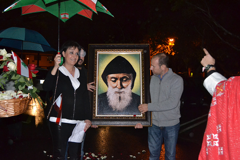 Llevando una imagen de San Sharbel, los feligreses de Nuestra Señora del Líbano van en procesión bajo la lluvia, para dar la bienvenida a la reliquia del santo libanés.