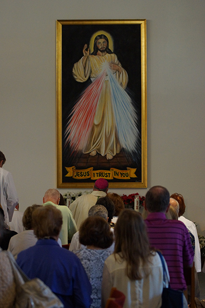 St. Coleman parishioners look on as Miami Auxiliary Bishop Peter Baldacchino blesses the painting of Divine Mercy created by a local Polish artist, Zbigniew Lazur.