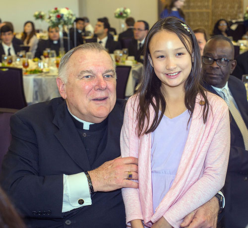 Archbishop Thomas Wenski poses for a photo with Nanni Chung-Vastine, 8, whose mother is Sui Chung, vice-president of the Catholic Legal Services board of trustees.