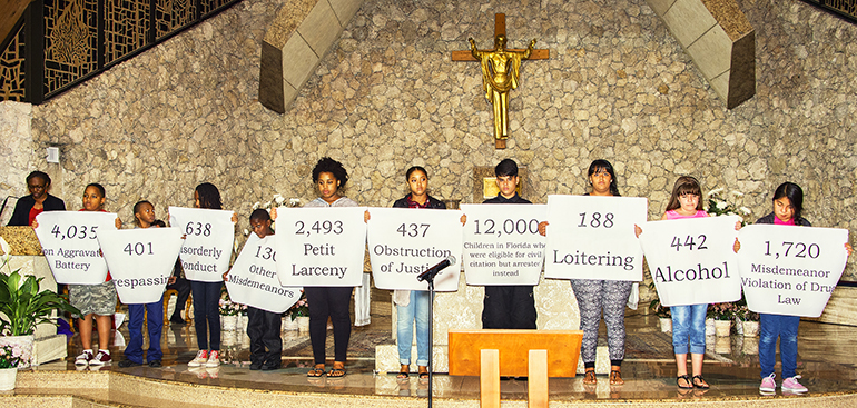 A group of children hold up signs for the numbers and types of offenses for which Florida children have been arrested over a one-year period.