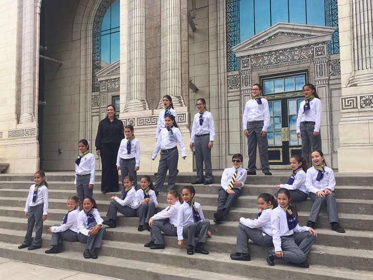 Members of St. Bonaventure's Children's Chorale and their director, Ysomar Granados, pose for a photo in front of a facade at Universal Studios in Orlando.