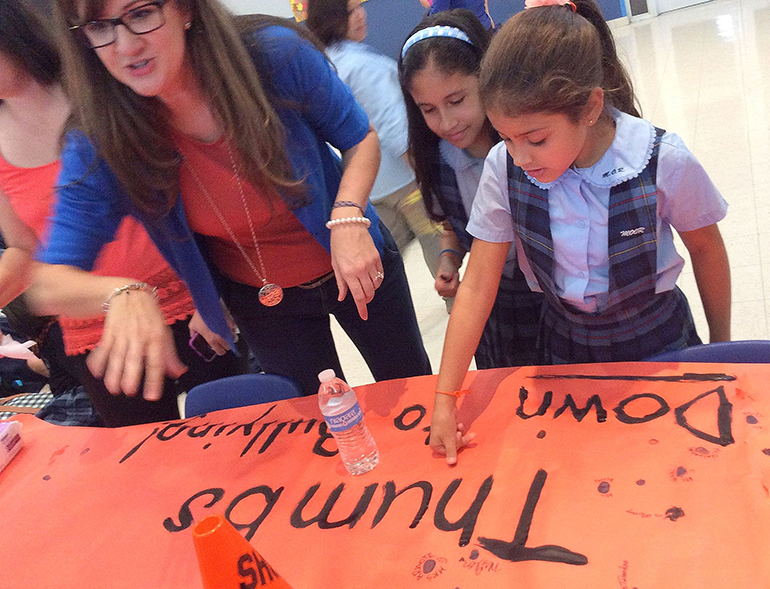 Students use their thumbprints to "sign" an anti-bullying poster at Mother of Our Redeemer School.