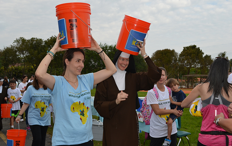 Eleonora Cacchiore, parent of students in fouth, second and kindergarten at St. Theresa School, walks while carrying a water pail alongside Carmelite Sister Emma Luz.