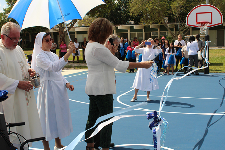 PTA President Toni Acocella cuts the ribbon inaugurating the new basketball court at the Marian Center. She was joined by Father Curtis Kiddy, who blessed the court, and Sister Fausta Rondena.