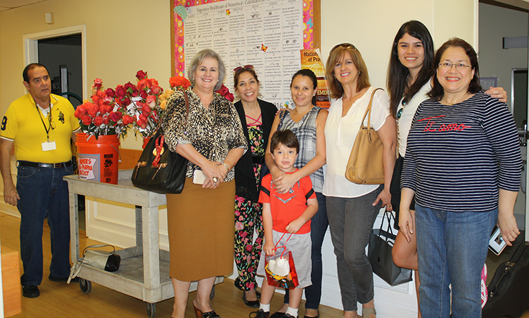 From left: Chaplain Manuel Ruda and musician Mirtha de la Torre, along with St. Patrick Emmaus women Michelle Oyanguren, Laura Devoto and son Ian, Adrianna Davis, Andrea Giron, and Chaplain Maria Meneses pose next to a handcart of roses ready to be delivered to the women at the Waterford Nursing Home in Hialeah.