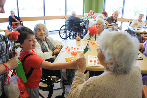 Six-year old Ian Devoto brings joy to Waterford Nursing Home resident Rafaela Sidron by handing her a long-stem rose in honor of Mother's Day. Looking on, from left, are Gariella Hernandez and Gaudencia Fernandez.