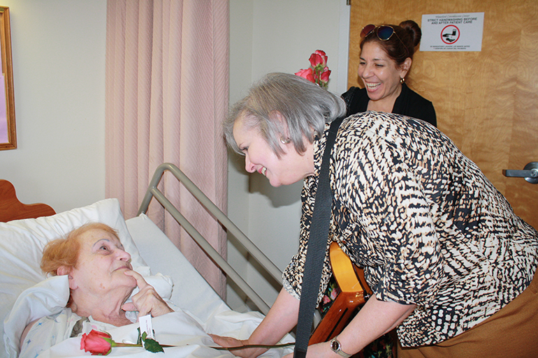 Guitarist Mirtha de la Torre, accompanied by Michelle Oyanguren of the St. Patrick Women's Emmaus, visits Waterford Nursing Home resident Raquel Aguila. "She can't speak but she speaks to me with her eyes," said Maria Meneses, Waterford chaplain and also a member of St. Patrick's Emmaus group. "She loves music and that's why she is fully awake and pensive and happy with de la Torre's singing."